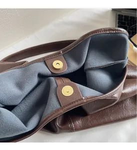 Detail view of gold magnetic buckles and gray fleece lining on a dark brown leather tote bag