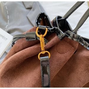 Détail du sac seau en daim marron avec poignée en cuir verni noir et ferrures dorées