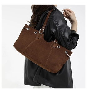 Close-up of brown suede tote bag with silver eyelets and adjustable strap on a model