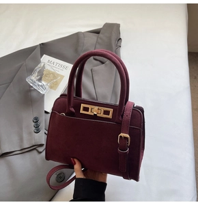 Close-up of a burgundy suede handbag featuring a gold metallic clasp and dual handles