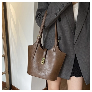 Detailed view of brown glossy tote bag with gold buckle on a grey plaid blazer outfit