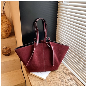 Detail of burgundy suede tote bag with knotted strap on wooden ledge by window