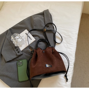 Détail d'un sac seau en daim marron avec garniture en cuir noir et logo métallique