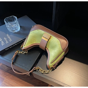 Close-up of green suede underarm bag featuring brown leather trim and golden chain strap