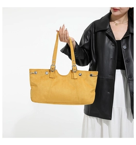 Detail of yellow suede tote bag featuring silver eyelets and adjustable shoulder strap