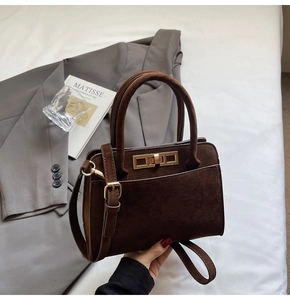 Detailed view of dark brown suede handbag with a golden twist-lock and top handle