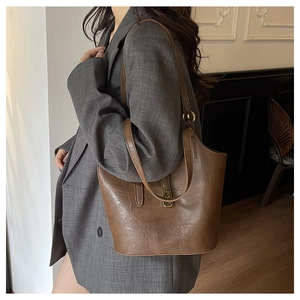 Detail view of brown leather bucket bag with gold lock on a model in a grey blazer