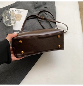 Detail view of dark brown leather handbag base featuring four gold protective metal feet