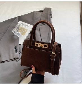 Detail view of brown suede handbag featuring a gold metal twist-lock and front pocket