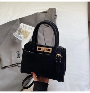 Close-up of black matte texture handbag with gold twist lock and elegant metal hardware