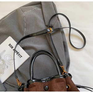 Détail du sac seau en daim avec bandoulières en cuir verni sur blazer gris