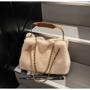 Detail of beige faux fur handbag with brown leather strap and golden chain on a book