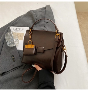 Detail of dark brown matte leather bag featuring a miniature charm and gold hardware