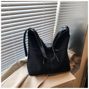 Détail du cabas en daim noir avec surpiqûres contrastées sur un trench-coat beige classique