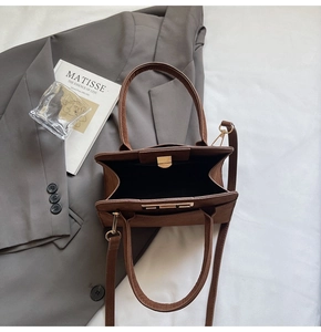 Top view of brown tote bag with adjustable strap next to an art book and grey blazer