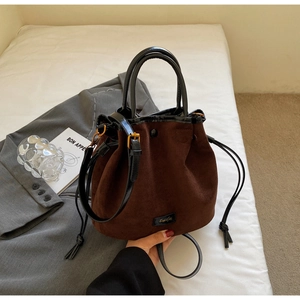 Détail du sac seau en daim marron foncé avec poignée en cuir noir et cordon de serrage doré