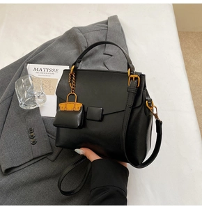 Detailed shot of black faux leather handbag with gold hardware and orange charm accessory