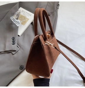 Detail of a brown suede handbag with a gold twist lock on a white fabric background