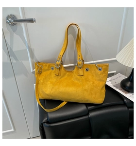Detail of yellow suede tote bag with silver eyelets and adjustable strap on a bench