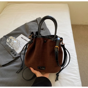 Détail du sac seau en daim marron café avec cordon en cuir noir et logo métallique doré