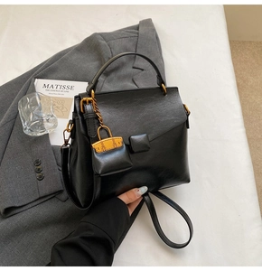 Detailed close-up of a black minimalist leather handbag with a mini bag charm accessory