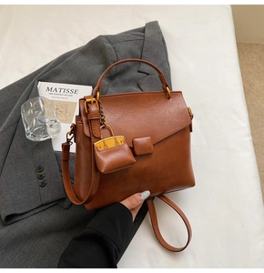Detail of caramel brown crossbody bag with mini charm and adjustable shoulder strap