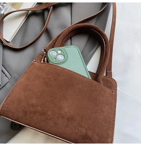 Detail of a large brown matte leather tote bag featuring slim straps and a phone compartment