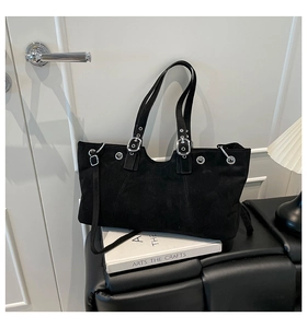 Detail of black suede tote bag featuring silver eyelets and adjustable punk style metal buckle