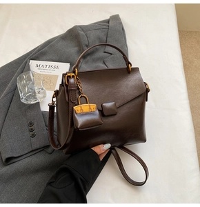 Detail of dark brown retro square handbag on grey blazer with decorative pendant