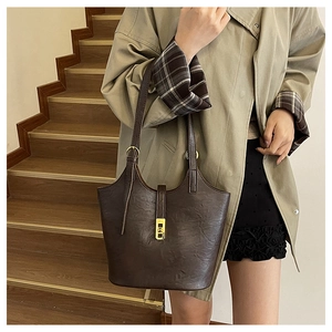 Detail of vintage brown leather tote bag with gold buckle on a model's shoulder