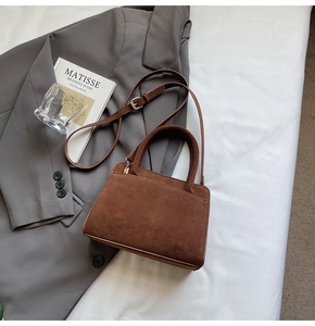 Detail view of the brown suede handbag showing texture, ring handles, and golden hardware