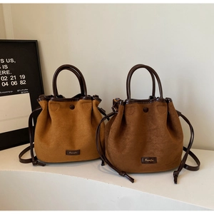 Détail du sac seau en daim avec fermeture à cordon et poignées en cuir marron