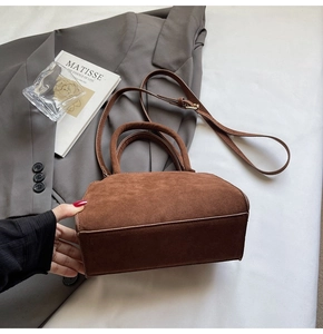 Detail of dark brown matte suede handbag showing twin handles and adjustable shoulder strap