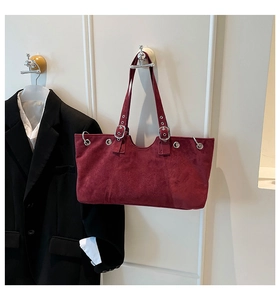 Close-up of vintage burgundy suede tote bag with silver metal buckle details on a white wall