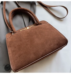 Detail of a brown suede handbag with golden rectangular lock and elegant trapezoidal structure
