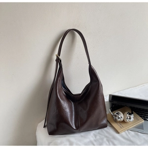 Detail showing high-capacity dark brown leather tote bag on bed with lifestyle accessories