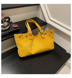 Detail of yellow suede tote bag featuring silver buckles and decorative metal eyelets
