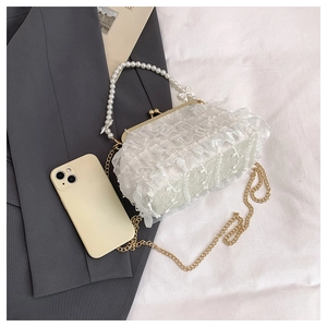 Détail du sac en dentelle blanche avec poignée en perles et nœud doré sur fond clair
