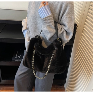 Detail of black faux fur shoulder bag with gold chain strap in a stylish indoor setting