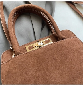 Detail of dark brown suede tote featuring golden rectangular twist lock and fine texture