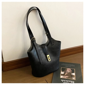 Detail of black embossed tote bag showing golden buckle and adjustable straps on wood floor