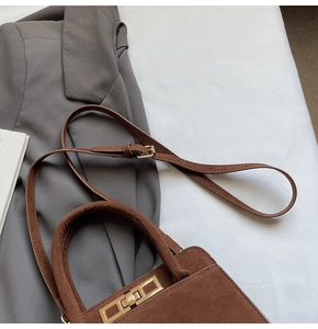 Close-up of a dark brown suede handbag featuring a gold rotary lock and leather strap