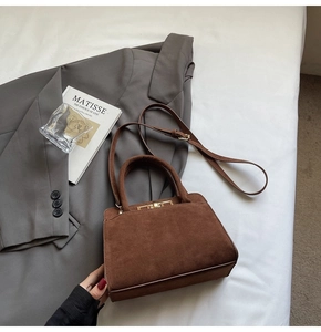 Close-up of brown suede trapezoid handbag featuring gold metal lock and leather texture