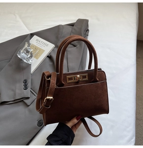 Detail of dark brown suede handbag featuring a gold twist lock and leather handle strap