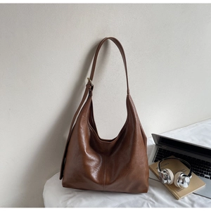 Detail of a dark brown hobo tote bag with glossy leather next to a laptop and headphones