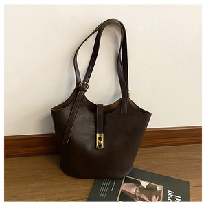 Detail of dark brown leather bucket bag featuring a long gold metal lock and fine texture