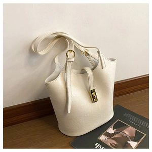 Detailed macro view of the cream leather bucket bag with gold metal lock and shoulder strap