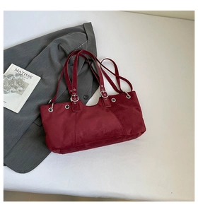 Detail of red matte suede tote bag with silver eyelets resting on a grey blazer