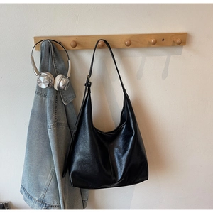 Detail of a black leather hobo tote bag hanging on a hanger with a casual outfit