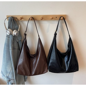 Detail view of large brown and black leather tote bags on hooks with a denim jacket